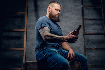 Studio portrait of bearded tattooed hipster male holds the beer