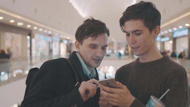 Two young man using smartphone in a shopping center. joyful guys watching video on tablet