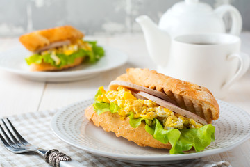 Sandwich stuffed with scrambled eggs, ham and lettuce leaves on a light wooden background. Selective focus.