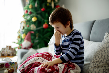 Little child, boy, blowing his nose and sneezing, lying sick in