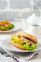 Sandwich stuffed with scrambled eggs, ham and lettuce leaves on a light wooden background. Selective focus.