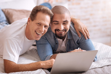 Fototapeta premium Positive gay couple lying on the bed and watching film