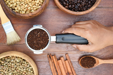 Freshly ground coffee beans in a metal filter and coffee beans with ground coffee in wooden spoon and cinnamon
