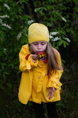 cheerful girl in a yellow raincoat blows a butterfly which sits on a hand on a spring day in the park