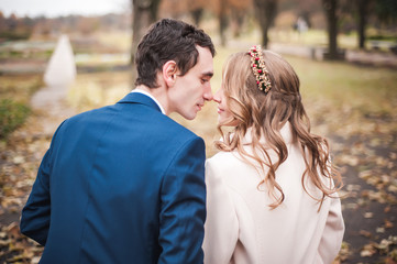 Newlyweds sit on the wooden bench in an autumn garden, back view