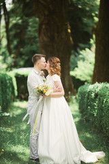 Stylish couple of happy newlyweds walking in the park on their wedding day with bouquet