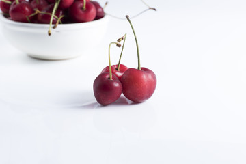 red cherries laid on a clear foreground and background cherries in a bowl.