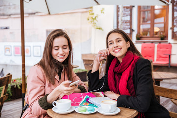 Two women listening to music from mobile phone in cafe