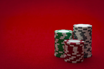 Casino and gambling concept with three stacks of chips of different colors ( red, green and white/ grey) isolated on a red felt with copy space