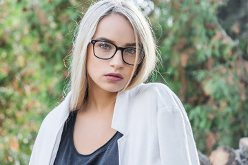 portrait of a young woman, blonde, glasses, outdoors in the park