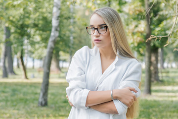 a young woman doctor, blonde in glasses in park outdoors