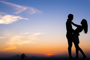 Silhouette of Happy Young Couple playing with cat Outside at Sunset
