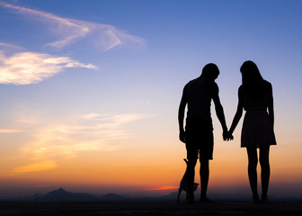 Silhouette of Happy Young Couple playing with cat Outside at Sunset