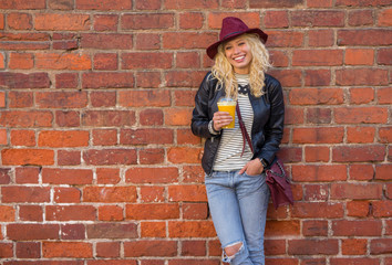 Modern woman standing by the brick wall with orange juice in her hands