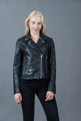 Portrait of a blond girl in a leather jacket gray studio backgro