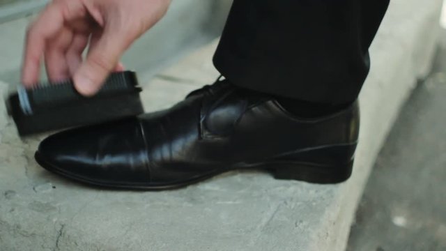 Businessman cleans shoes black shoe polish at the summer street