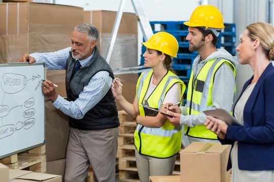 Manager and warehouse workers discussing over whiteboard - Powered by Adobe