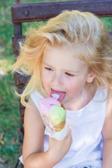 Little girl eats big ice-cream in the park.