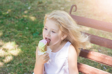 Little girl eats big ice-cream in the park.