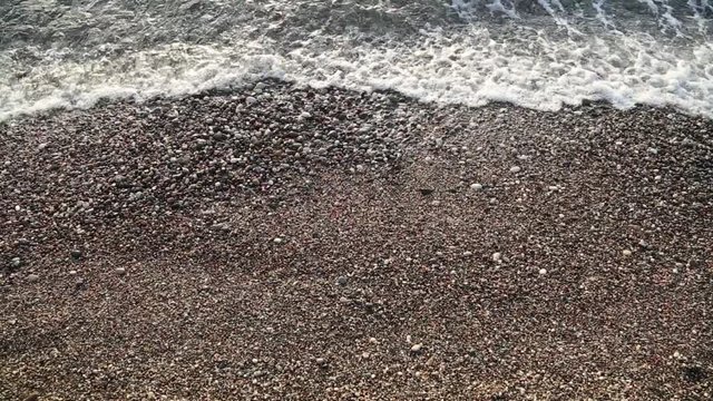 Sparkling sea water waves surface over many stones of seashore. Real time full hd video footage.
