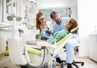 Medical dentist team in dental office talking with female patient and preparing for treatment.