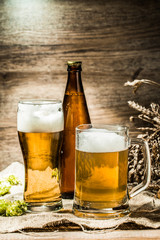 Mug, glasse, bottle of beer with foam on wooden background