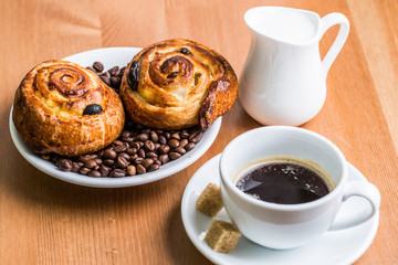 Coffee cup with cinnabon and milk jug on wooden background.