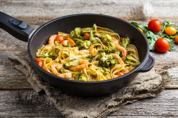 Pasta linguine with shrimps and broccoli in dripping pan on wooden background.