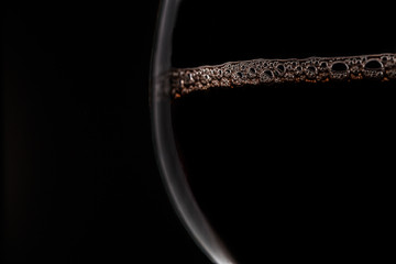 Red wine with bubbles in glass on black background