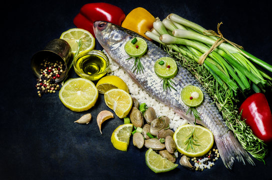 Delicious fresh fish on dark vintage background.Fish with organic vegetables,olive oil, mixed pepper, and fresh clams.Top view.Healthy clean food concept.