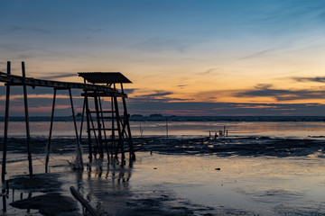 Golden Hour moment,beautiful tropical sunset background, wooden water pump tower on the muddy beach. cloudy and yellow sky.surface level shot.low tide sea view
