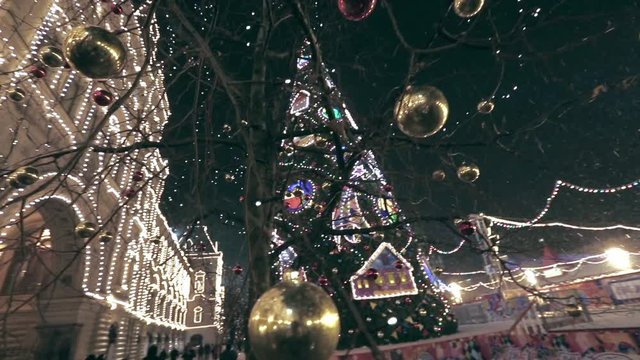 Christmas street decoration. Building, trees in garlands. Red and yellow decorative balls hanging on the trees against background with illuminated building. Beautiful Christmas Balls.
