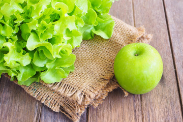 Top view of green oak lettuce and green apple on a wooden table.