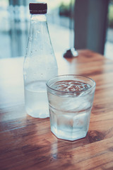 Glasses with ice cubes and water bottles on wooden table