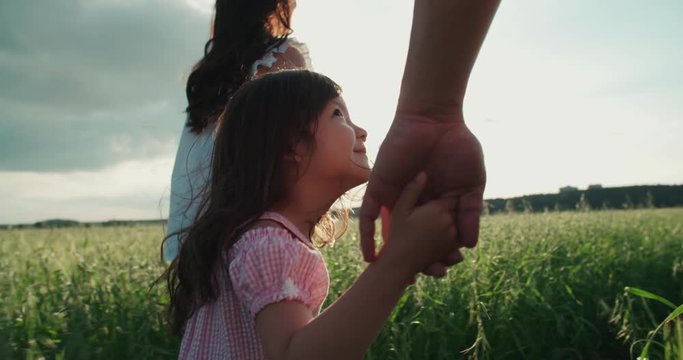little Asian girl walking on the green field with their parents, holding the hand of his father, slow motion
