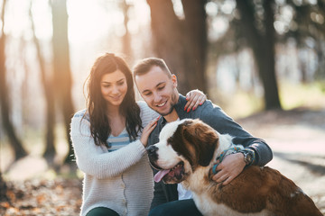 People and dogs. Young couple enjoying nature or park outdoors together with their  adorable Saint Bernard puppy.