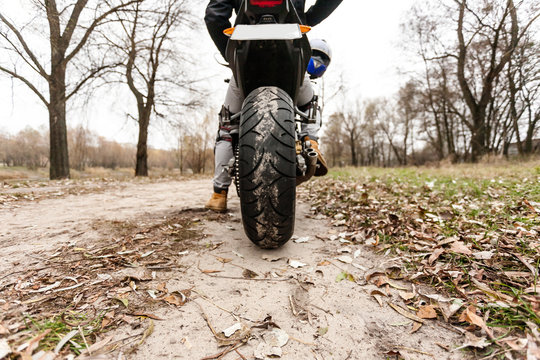 Biker sitting on motorcycle on an empty road, close-up view on rear wheel.