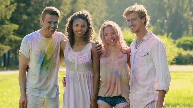 Young friends covered in holi colors, happy people hugging and smiling to camera