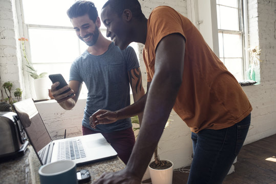 Two smiling young men with cell phone and laptop in a loft