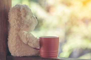 Teddy bear alone with red coffee cup on wooden table - 128992408