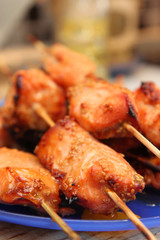 Skewers of salmon with honey and sesame seeds on a blue plate.