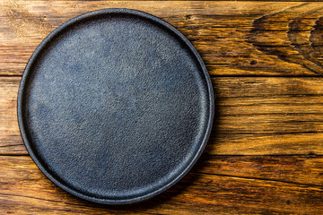 Empty rustic black cast iron plate over old wooden background