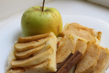 Delicious crumbly apple pie near garden apple with cinnamon stick on a white plate on a white window sill