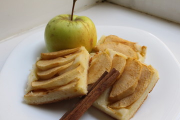 Delicious crumbly apple pie near garden apple with cinnamon stick on a white plate on a white...