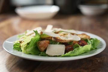 plate with fresh caesar salad with chicken on old wooden table, shallow focus