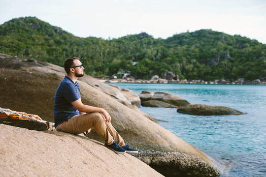 Male IT specialist in glasses sitting on sea beach enjoying outdoors