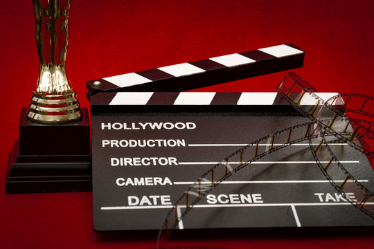 Hollywood Film Awards Concept With Shiny Metallic Movie Award Wrapped In Celluloid Film Strip On Red Carpet With Clapper Board