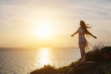 Fototapeta na wymiar Beautiful free happy woman in white dress enjoying the golden sunshine glow of sunset with arms outspread, serenity in nature. Enjoyment, wind in blond hair