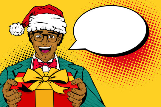 Wow Christmas pop art man. African man in Santa Claus hat, suit and glasses with smile holding gift box and empty speech bubble. Vector illustration in retro comic style. New year party invitation.