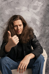 Handsome casual fashion man with long hair sitting on chair showing the thumbs up gesture